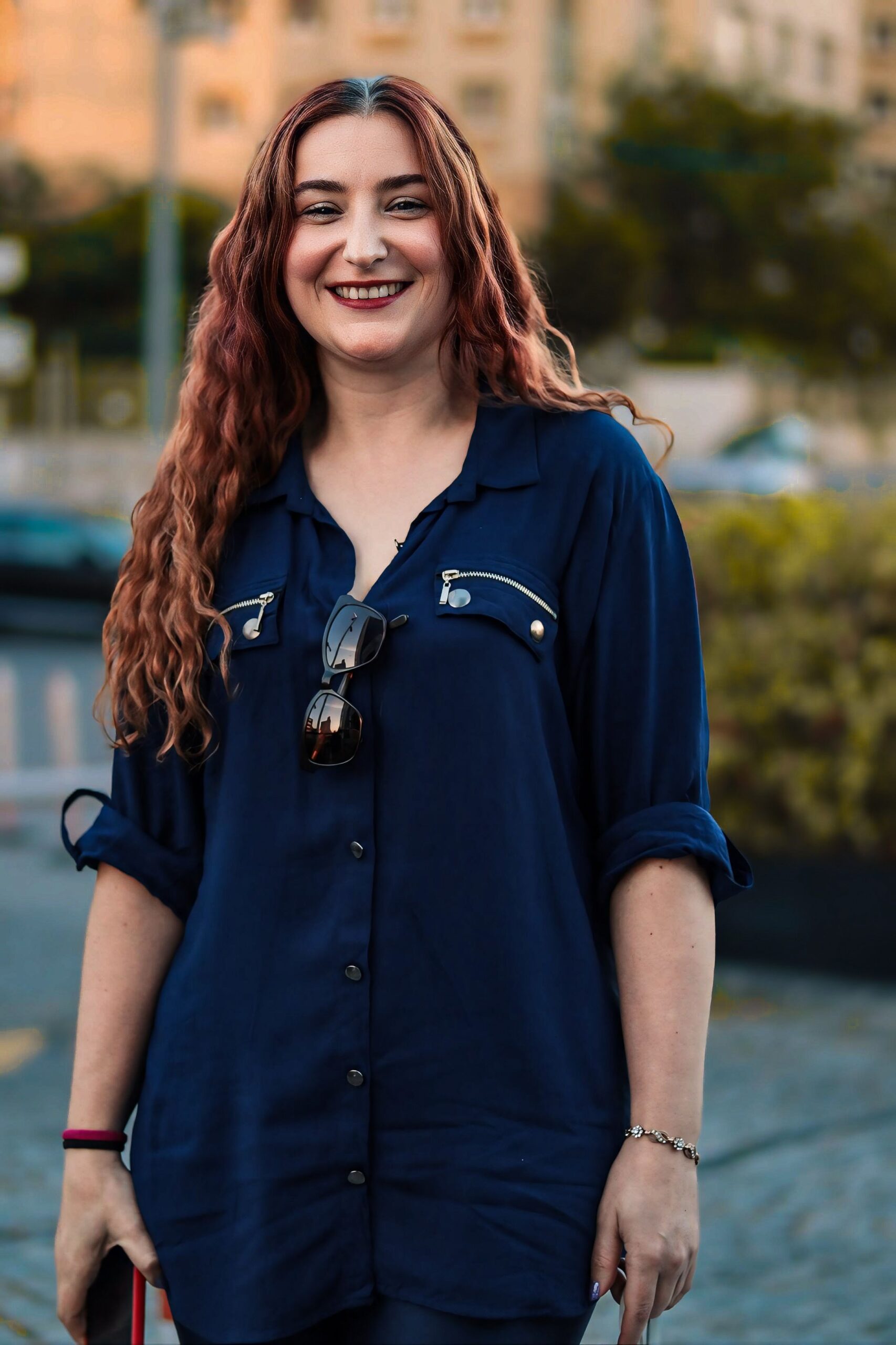 A cheerful woman with wavy hair smiles in an urban park. Captured outdoors.